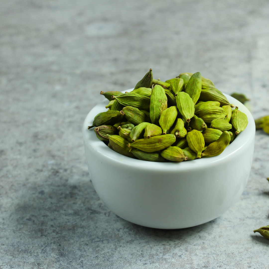 Green cardamom pods in a white bowl on a gray surface